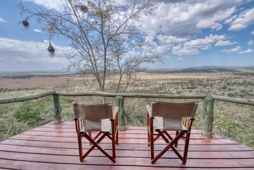 two chairs on a wooden deck with a view of the desert at Mbali Mbali Soroi Serengeti Lodge in Banagi