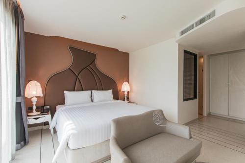 a bedroom with a large white bed and a chair at Rachabhura Hotel in Ratchaburi