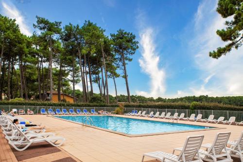 a swimming pool with lounge chairs and a body of water at SOWELL Family Pignada Plage in Soustons