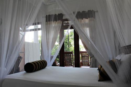 a bedroom with a bed with white curtains and a window at Amado Homestay Ella in Ella