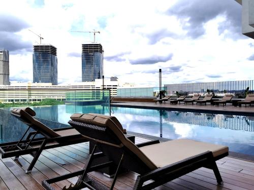 a swimming pool with two lounge chairs on top of a building at Mid Valley Southkey Mosaic Cozy Suite at Johor Bahru in Johor Bahru