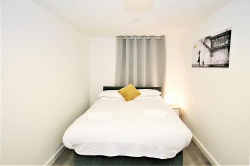 a bedroom with a white bed with a yellow pillow at The Aldgate Rooms in London