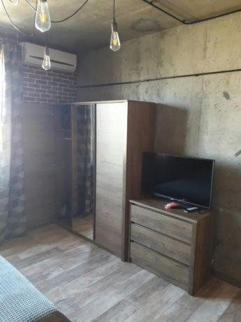 een kamer met een tv op een houten dressoir met een tvicterictericter bij ОДНОКОМНАТНЫЙ ЛОФТ НА 26 ЭТАЖЕ in Odessa
