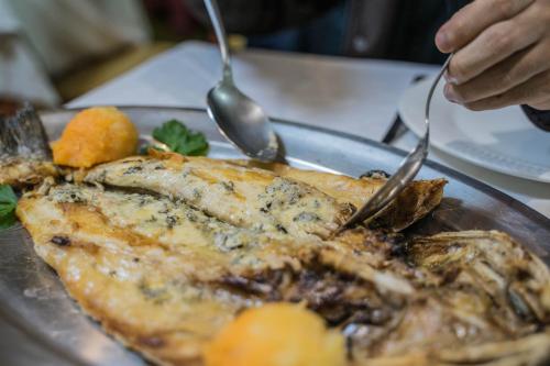 a person cutting a fish on a plate with forks and spoons at Gran Hotel Rural Cela in Belmonte de Miranda