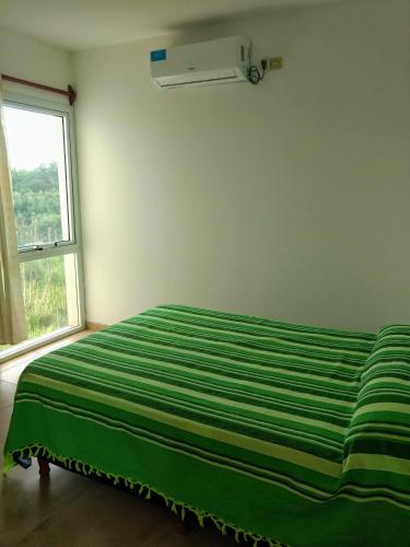 Cama verde en habitación con ventana en Alquileres Temporarios Villa María en Villa María