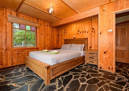 ein Schlafzimmer mit einem Bett in einem Holzzimmer in der Unterkunft Saintys Creek Cottage in South Bruny