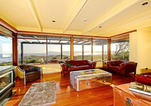 a living room with leather furniture and large windows at Cloudy Bay Villa in South Bruny