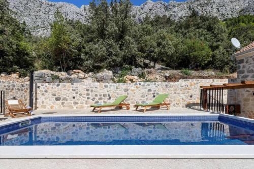 - une piscine avec 2 chaises vertes et un mur de roche dans l'établissement Holiday home Marijana, à Zaostrog