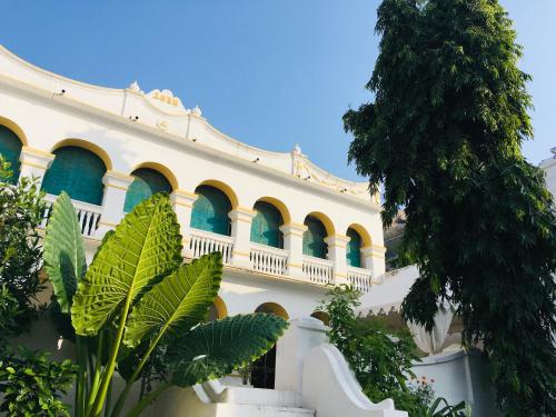 a white building with blue windows and a tree at Rawla Bisalpur in Jawāi Bāndh