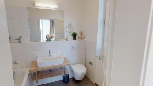 ein Badezimmer mit einem Waschbecken, einem WC und einem Spiegel in der Unterkunft Südkap C-06 in Pelzerhaken