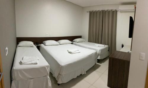 a hotel room with two beds and a television at Hotel Tainá - Aeroporto Cuiabá in Várzea Grande
