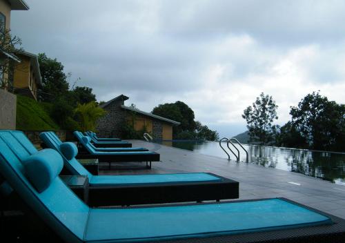 a pool with blue lounge chairs and a swimming pool at Poetree Thekkady in Thekkady