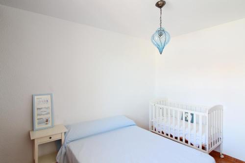 a white bedroom with a crib and a chandelier at Global Properties, Adosado en la playa con piscina in Sagunto