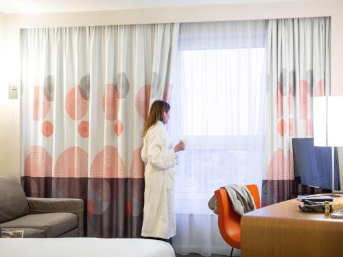 a woman in a robe looking out of a window at Novotel Reading Centre in Reading