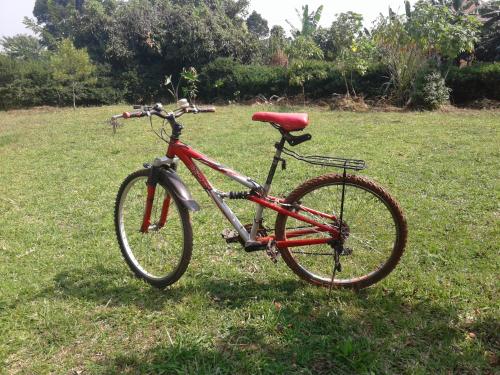 a red bike parked in the grass in a field at Plastic Bottles House in Entebbe