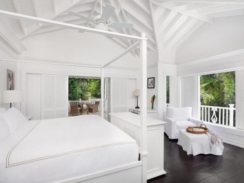 a white bedroom with a bed and a chair at Sugar Beach, A Viceroy Resort in Soufrière