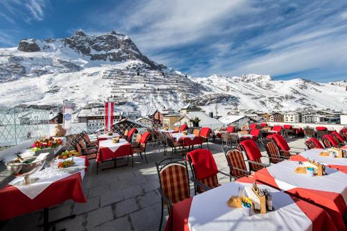 a restaurant with tables and chairs in front of a mountain at Hotel Enzian in Zürs am Arlberg