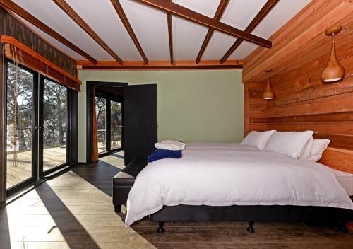 - une chambre avec un grand lit dans une pièce dotée de fenêtres dans l'établissement Taylors Bay Cottage, à South Bruny