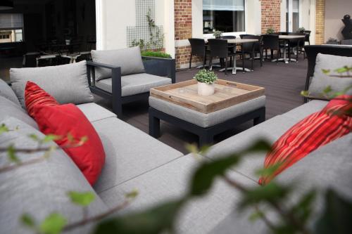 ein Sofa mit roten Kissen und einem Tisch auf der Terrasse in der Unterkunft Ambassador Hotel in De Panne