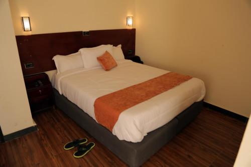 a bedroom with a large bed with white sheets and an orange pillow at Obelisk Hotel Axum in Āksum