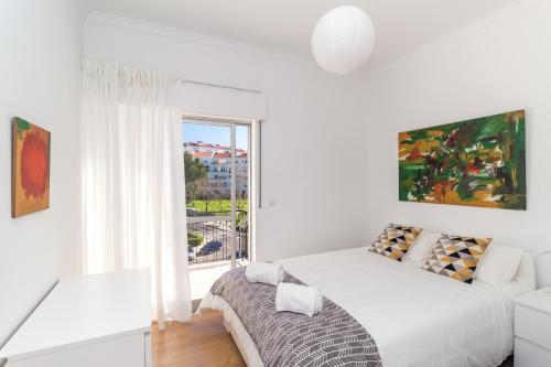 a white bedroom with a bed and a window at White Apartment - T2 near Beach in São João do Estoril