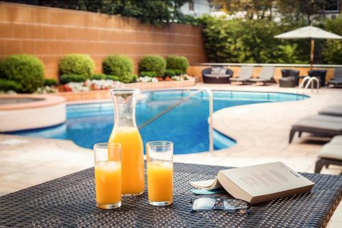 two glasses of orange juice on a table near a pool at Boulevard Suites Ferrat in Santiago