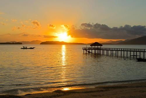 a sunset over the water with a pier and a boat at Cocotinos Sekotong Lombok in Sekotong