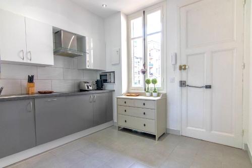 une cuisine avec des placards blancs, une fenêtre et une porte dans l'établissement Résidence Estienne d'Orves, à Nice