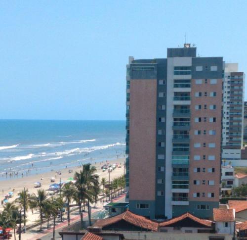 a tall building next to a beach with palm trees at Apartamento Temporada pé na areia in Mongaguá