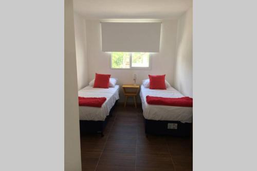 um quarto com 2 camas com almofadas vermelhas e uma janela em Apto céntrico con wifi em Colônia do Sacramento