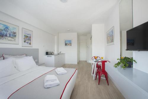 a white bedroom with a white bed and a red chair at Kitieos Apartments in Larnaca