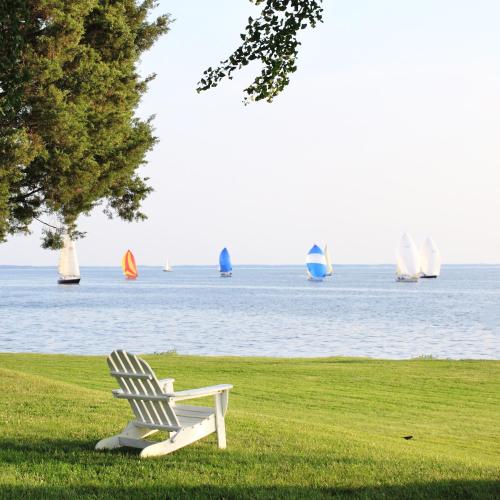 a white chair sitting in the grass with sailboats in the water at Sandaway Suites & Beach in Oxford