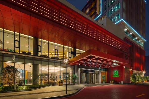 a large building with a red facade at night at Holiday Inn Chengdu Airport by IHG - Free Shuttle to Shuangliu International Airport in Chengdu