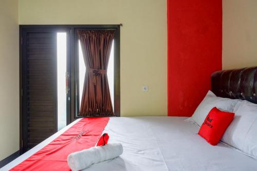 a bedroom with a red and white bed with a window at RedDoorz @ Gerbang Dieng Plateau Area in Wonosobo