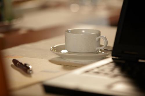 a white coffee cup sitting on a table next to a laptop at Hotel Restaurant Lüdenbach in Overath
