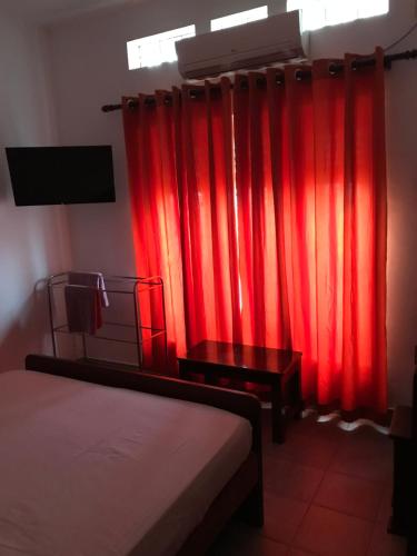 a bedroom with red curtains and a bed and a television at Dions Guest House in Negombo