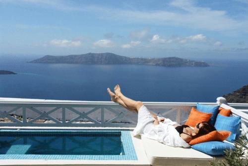 a man laying on a couch next to a swimming pool at Ellinon Thea Boutique Hotel in Firostefani