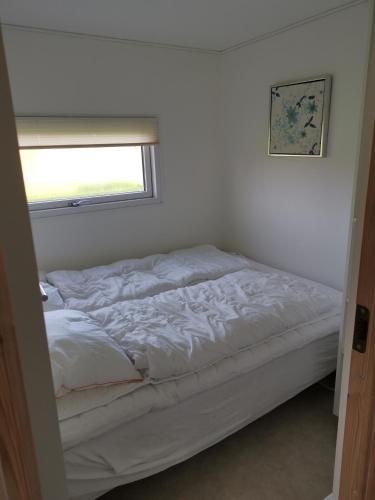 an unmade bed in a room with a window at Tangsø Hytteby in Bækmarksbro