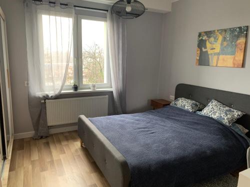a bedroom with a bed with a blue blanket and two windows at Apartament „Ogrodowa” in Bolesławiec