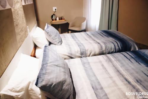 two beds in a hotel room with a chair at Bosveldrus Gastehuis in Vaalwater