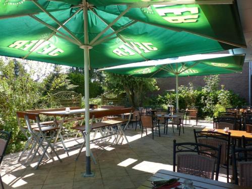 a patio with tables and chairs under a green umbrella at Hotel Deichgraf in Cuxhaven