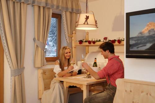 a man and a woman sitting at a table with wine glasses at Romantik Villa Cesanueva in Selva di Val Gardena