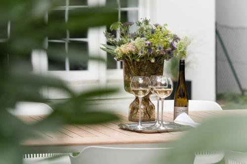 a table with two wine glasses and a vase with flowers at stilwerk Hotel Heimhude in Hamburg