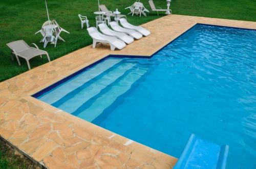 une grande piscine avec des chaises blanches et une table dans l'établissement Pousada Chalés da Felicidade, à Itu