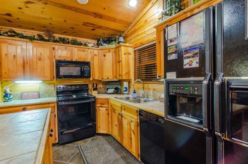 een keuken met houten kasten en zwarte apparaten bij Crooked Pine with Swing and Hot Tub in Broken Bow