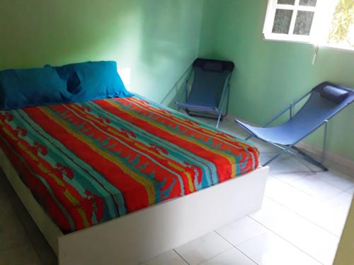 a bedroom with a colorful bed and two chairs at Villa Grandes pièces in Petit-Bourg