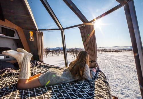 a woman laying on a bed in a tent in the snow at Peace & Quiet Hotel in Jokkmokk