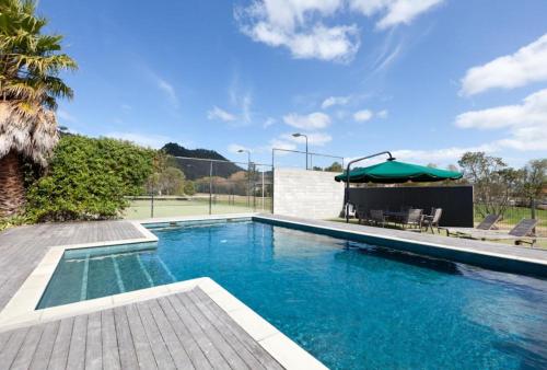 una piscina de agua azul y una sombrilla en Pauanui Pines Motor Lodge, en Pauanui