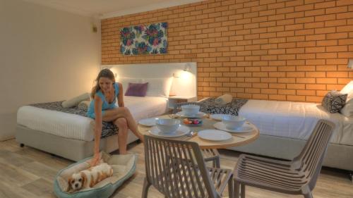 a girl sitting on a bed with a dog on a table at Rosebourne Gardens Motel in Woolgoolga