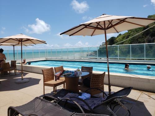 una piscina con sillas y sombrillas, una mesa y una piscina en Flet Beira-mar, Blue Sucet, en João Pessoa